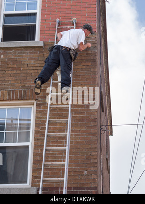 Ausgleich für Ziegel und Mörtel Reparatur. Balancieren hoch oben auf einer Leiter ein Mann repoints den Mörtel auf einem Backsteingebäude in Québec (Stadt). Stockfoto