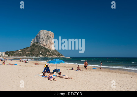 Die imposante Penyal d'lfac Felsen in der Bucht von Calp, Costa Brava, Spanien, mit Leuten am Strand im Vordergrund. Stockfoto