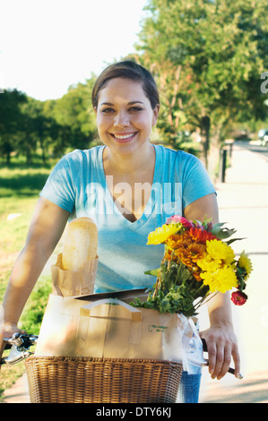 Gemischte Rassen Frau Reiten Fahrrad mit Blumen im Korb Stockfoto