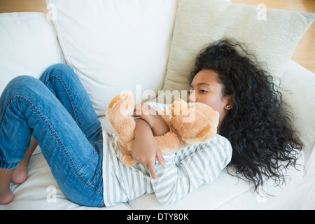 Gemischte Rassen Mädchen umarmt Teddybär auf sofa Stockfoto