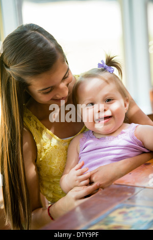 Hispanischen Mädchen halten Kleinkind Schwester am Tisch Stockfoto