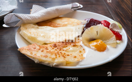 Gebratene Pfannkuchen auf weisse Teller und dunklen Hintergrund mit Sahne, Erdbeere, Ananas und Marmelade Stockfoto