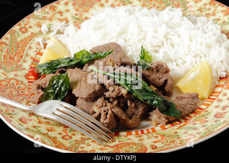 Chili-Rindfleisch mit knusprig gebratenen Basilikumblätter, serviert mit weißen Basmati-Reis und Zitrone-Keile. Stockfoto