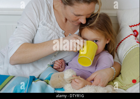 Mutter kümmert sich um ihre kranke Tochter, Verzicht auf heißen Tee, Mädchen im Bett liegend Stockfoto