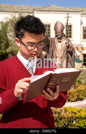 Ein uniformierter asiatisch-amerikanische Schüler liest die Bibel auf dem Campus eine private katholische High School in San Juan Capistrano, Kalifornien. Stockfoto