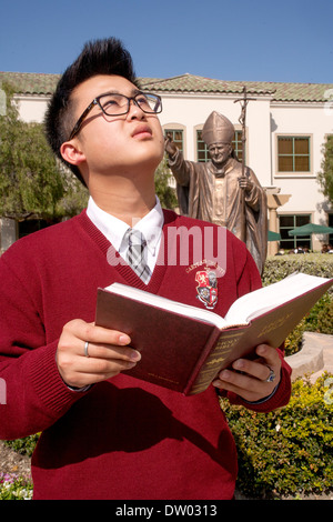 Ein uniformierter asiatisch-amerikanische Schüler liest die Bibel auf dem Campus eine private katholische High School in San Juan Capistrano, Kalifornien. Stockfoto