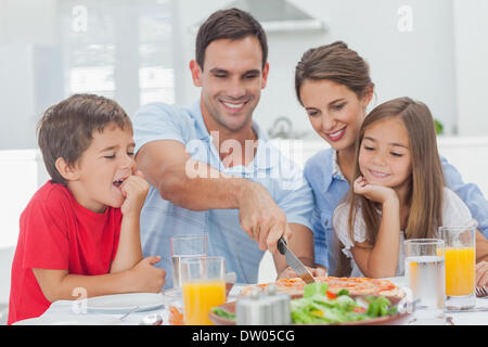 Man schneidet eine Pizza für seine Familie Stockfoto