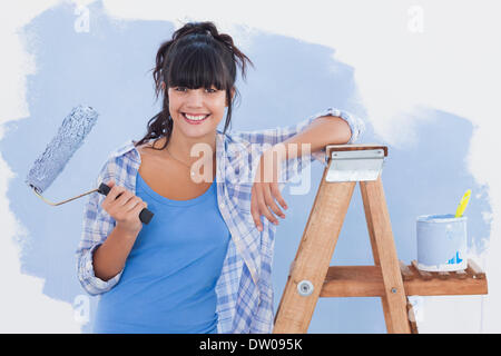 Frau mit Farbroller stützte sich auf Leiter Stockfoto