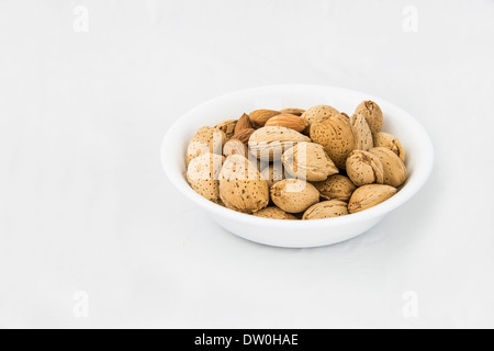Eine kleine Schüssel geschälte und ungeschälte Mandeln, isoliert auf weiss. Stockfoto