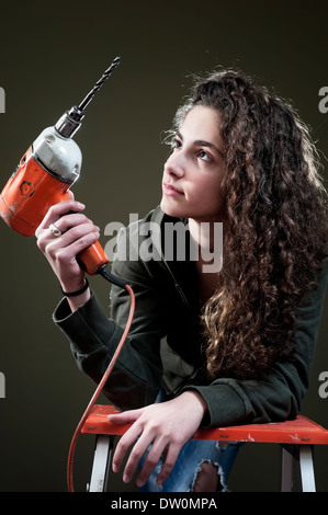 Junge Frau auf Leiter mit Bohrer arbeiten Stockfoto