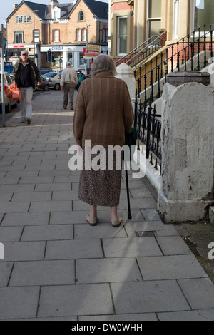 Rückansicht der alten Dame zu Fuß mit einem Stick unterstützt Stockfoto