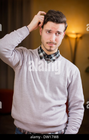 Verwirrt oder zweifelhafte junger Mann kratzte sich am Kopf und blickte. Drinnen in einem Wohnzimmer erschossen Stockfoto