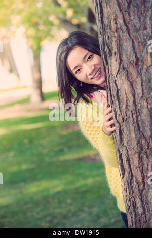 Frau versteckt sich hinter einem Baum Stockfoto