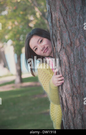 Frau versteckt sich hinter einem Baum Stockfoto