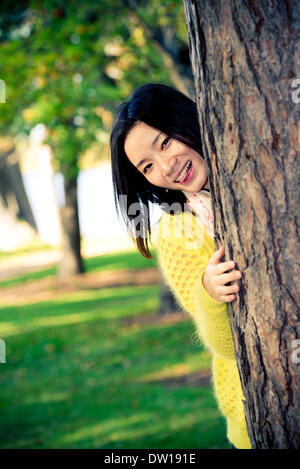 Frau versteckt sich hinter einem Baum Stockfoto