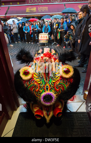 Löwe-Tänzerin aus der London Chinatown Chinese Association bitten um Angebote in der Tür des Feng Shui Inn an Chinese New Year, Gerrard Street, London, England Stockfoto