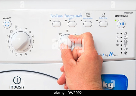 Kaukasischen Mann Hand anpassen ein Temperaturregler auf eine Indesit Waschmaschine, UK-Modell veröffentlicht Stockfoto