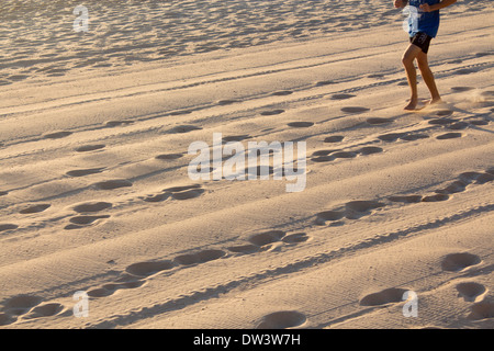 Fußspuren und Reifenspuren im Sand in der Morgendämmerung mit Läufer in der oberen Ecke des Rahmens Norden Steyne Strand Manly Sydney NSW Australia Stockfoto