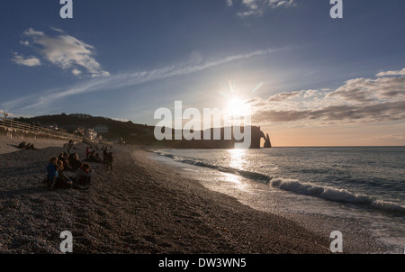 Menschen in Etretat Strand, beobachten den Sonnenuntergang über der Porte d'Aval, eine natürliche Arche in Etretat Kliffen, Klippen, Stockfoto