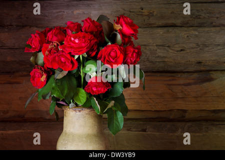 Schöne Rosen mit frischen und welk Knospen in Keramik Krug auf rustikalen hölzernen Stab Hintergrund Stockfoto
