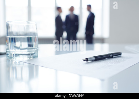 Bild Geschäftsdokument, Stift und Glas Wasser am Arbeitsplatz mit Kollegen auf Hintergrund Stockfoto