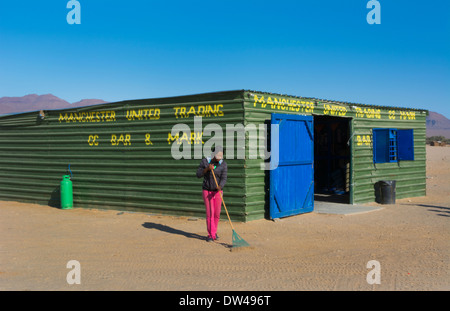 Namibia Afrika Puros Dorf Frau fegt Sand vor Ort Bar genannt Manchester United Stockfoto