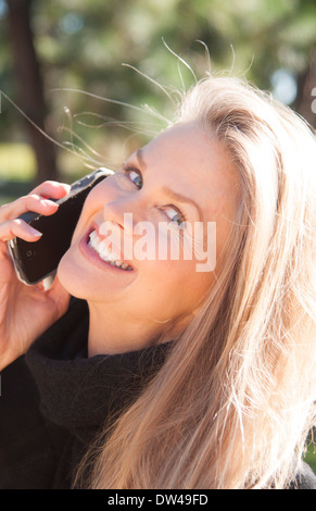 junge attraktive 50 Jahre alte Frau am Handy lächelnd im Freien noch schöner noch im mittleren Alter Stockfoto