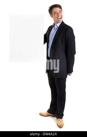 Dapper Geschäftsmann mit einem käsigen Grinsen hält eine rechteckige leeres weißes Schild mit Exemplar für Ihren Text auf Armlänge Stockfoto