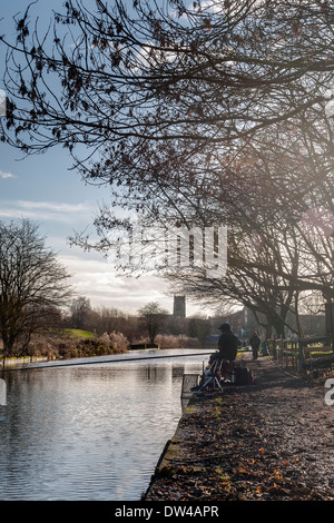 Fischer und Wanderer am Kanal in Middlewich, Cheshire, mit Pfarrkirche im Hintergrund und Winter Bäume im Vordergrund. Stockfoto