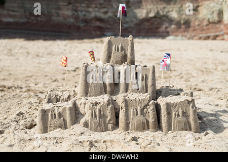 An einem Sandstrand eine Sandburg gekrönt mit der Welsh national andere britische Flaggen Stockfoto