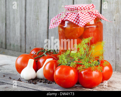 Hausgemachte Tomaten im Glas. Frische und konservierte Tomaten auf Holzbrett Stockfoto