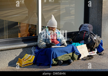 Bärtige Obdachloser auf dem Bürgersteig sitzen und dabei ein Kreuzworträtsel auf Granville Street, Vancouver, BC, Kanada Stockfoto