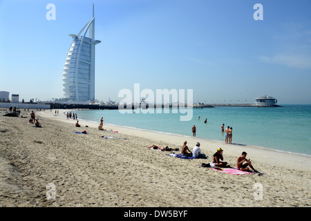 DUBAI - Urlauber genießen Sie den öffentlichen Strand im Schatten des berühmten Burj Al Arab Hotel am Arabischen Meer Stockfoto