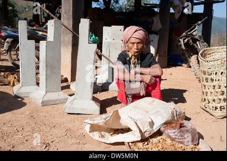 Karen Hill Tribe Frau sitzt, raucht eine Pfeife in der Nähe einer Plünderung Bohnen vorbereiten. Stockfoto