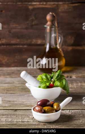 Mischung aus Oliven mit frischem Basilikum in weißem Mörtel und Vintage Flasche Olivenöl auf alten Holztisch Stockfoto