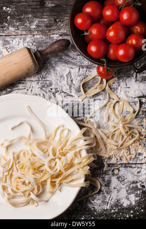 Draufsicht auf Raw hausgemachte Pasta mit Tomaten und Mehl über alten Holztisch Stockfoto