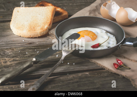 Frühstück mit Spiegelei auf Pfanne serviert mit Toast, red hot Chili Peppers und Vintage Geschirr über alten Holztisch
