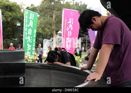 Taipei, Taiwan - 28. Februar 2014: junger Mann und seine Schwester lehnte sich an die Urne, die Knochen der Opfer unter 228 Denkmal in Trauer beim Jubiläum des 1947 Massaker, denen Tausende von nationalistischen Kuomintang-Truppen aus China, an der Taipei Peace Park am 28. Februar 2014 getötet wurden dargestellt. Das Massaker blieb für Jahrzehnte unter der späten nationalistischen KMT Führer Chiang Kai-shek der Regel Tabu. Es war nicht bis 1995, dass die damaligen Präsidenten Lee Teng-Hui die erste offizielle Entschuldigung gemacht. Parlament später vereinbart, die Opfer zu entschädigen und 28 Februar ein offizieller Feiertag. Stockfoto