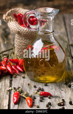 Glasflasche Olivenöl mit rote scharfe Chilischoten über alten hölzernen Hintergrund. Stockfoto