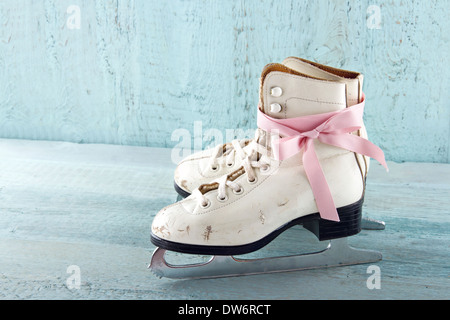 Paar weiße Frauen Schlittschuhe auf blauen Vintage Holz-Hintergrund mit rosa Schleife Stockfoto