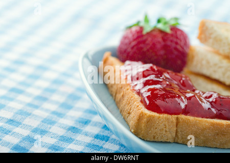 Toastscheiben mit roten Erdbeer-Marmelade und frischen Beeren auf blauen Vintage-Hintergrund Stockfoto