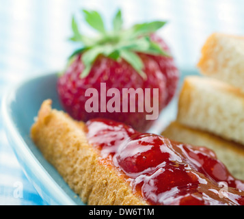 Toastscheiben mit roten Erdbeer-Marmelade und frischen Beeren auf blauen Vintage-Hintergrund Stockfoto