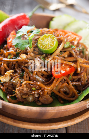 Indonesischen und malaysischen Küche, mi Goreng oder mich Goreng Mamak, würzig gebratene Nudeln mit Esstisch aus Holz. Frisch heiß mit gedünstetem Rauch. Stockfoto