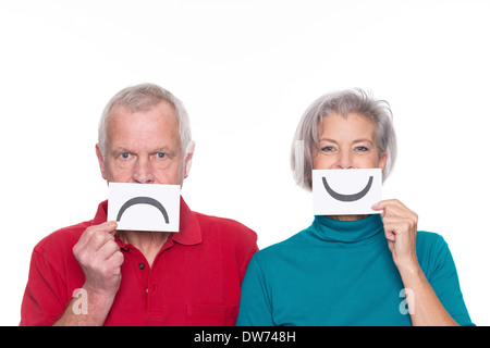 Älteres Paar mit Smiley und unglücklich Zeichen vor weißem Hintergrund Stockfoto