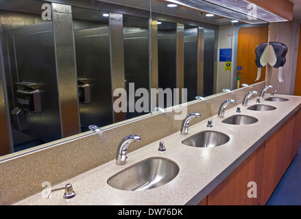 Eine Reihe von Waschbecken und Metallständen, die sich in den Spiegeln eines Fährschiffes spiegeln. Automatische Wasserhähne für mehr Sauberkeit. Stockfoto