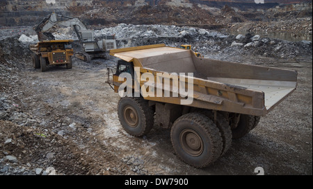 Caterpillar Muldenkipper wartet in der Schlange, während ein Liebherr-Bagger Erz in einem LKW im Hintergrund lädt Stockfoto