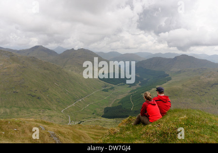 Ein junges Paar saß auf einem Berggipfel in den schottischen Highlands rot gekleidet Stockfoto