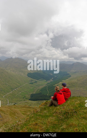 Ein junges Paar saß auf einem Berggipfel in den schottischen Highlands rot gekleidet Stockfoto