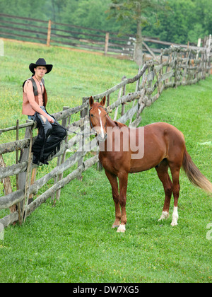 Mann in Cowboy Kleidung sitzt auf dem Zaun neben dem Pferd Stockfoto