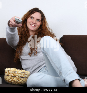 Junge Frau auf einem Sofa sitzt, vor dem Fernseher und Essen popcorn Stockfoto